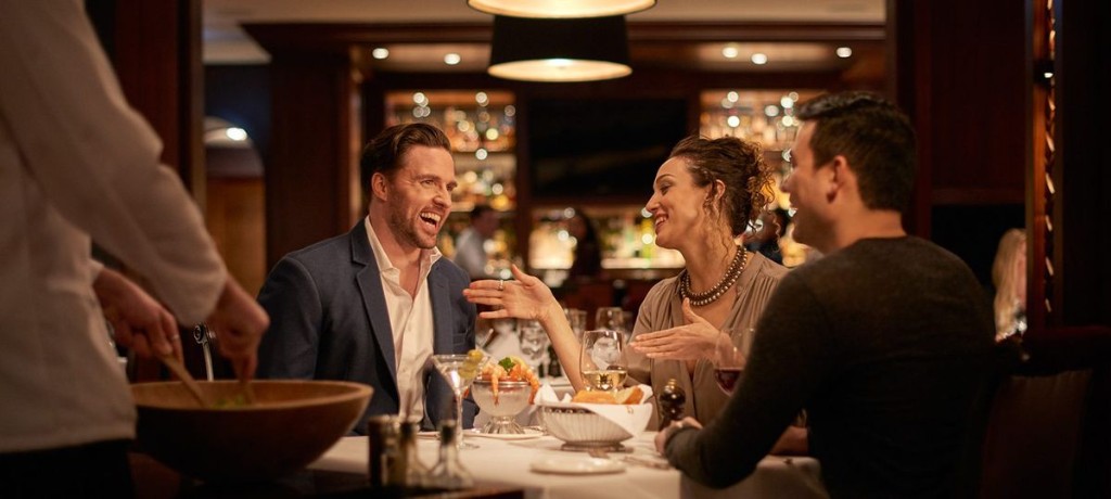 Friends laughing over dinner at Pera Palace while a waiter serves at the table